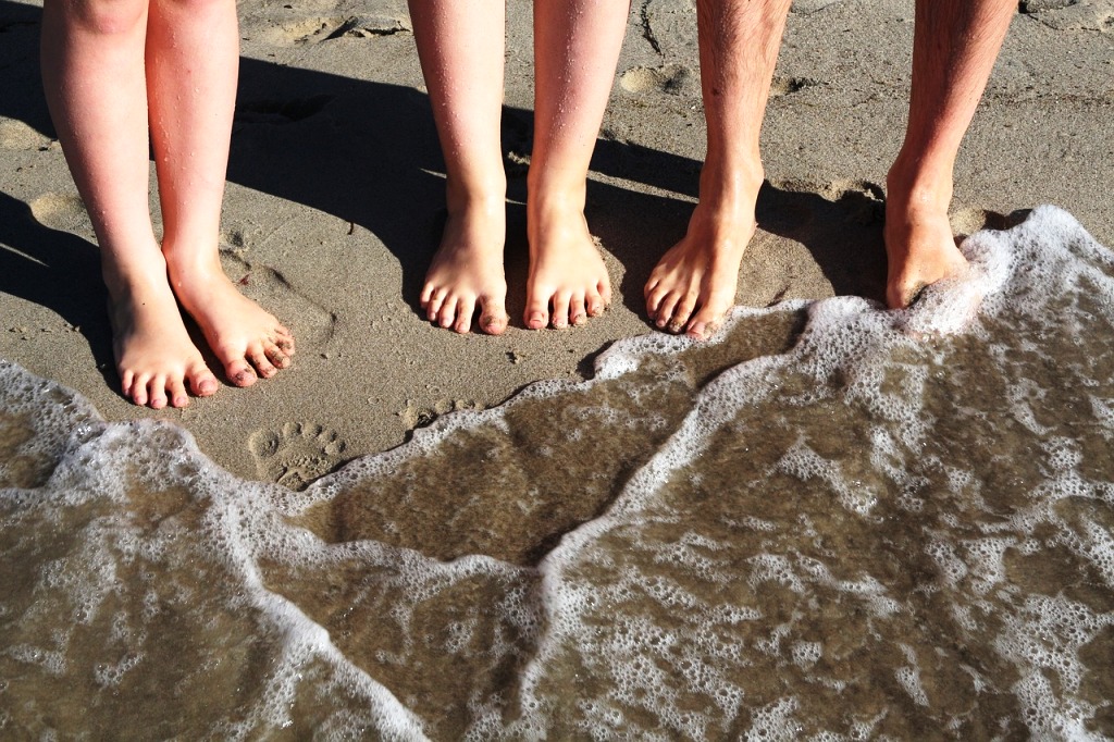 Three pairs of bare feet on a sandy beach beside the sea